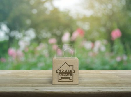 Martillo y llave inglesa con el icono de la casa en el cubo del bloque de madera en la mesa de madera sobre la flor rosa borrosa y el árbol en el parque, concepto de servicio a domicilio de negocios