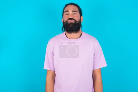 Foto de Retrato de encantador hombre caucásico divertido con barba vistiendo camiseta violeta sobre fondo azul enviando beso de aire - Imagen libre de derechos