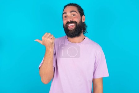 Téléchargez les photos : Homme caucasien impressionné avec barbe portant T-shirt violet sur fond bleu point de retour espace vide - en image libre de droit