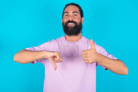 Photo for Caucasian man with beard wearing violet T-shirt over blue background showing thumb up down sign - Royalty Free Image