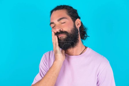 Téléchargez les photos : Homme caucasien avec barbe portant T-shirt violet sur fond bleu avec mal de dents - en image libre de droit
