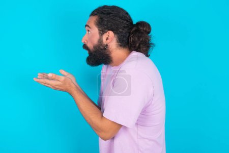 Photo for Profile side view view portrait of attractive Caucasian man with beard wearing violet T-shirt over blue background sending air kiss - Royalty Free Image