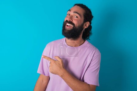 Téléchargez les photos : Homme caucasien avec barbe portant T-shirt violet sur fond bleu joyeux démontrant copie espace look nouveauté - en image libre de droit