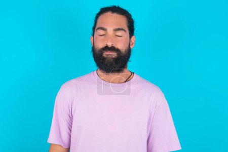 Téléchargez les photos : Homme caucasien avec barbe portant T-shirt violet sur fond bleu beau charmant mignon attrayant beau winsome doux yeux fermés paisibles - en image libre de droit