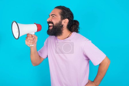 Photo for Funny Caucasian man with beard wearing violet T-shirt over blue background  People sincere emotions lifestyle concept. Mock up copy space. Screaming in megaphone. - Royalty Free Image