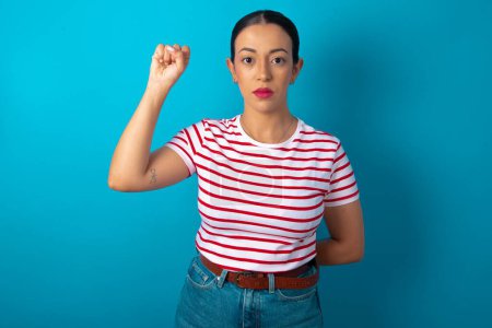 Foto de Mujer vistiendo una camiseta a rayas sintiéndose seria, fuerte y rebelde, levantando el puño, protestando o luchando por la revolución. - Imagen libre de derechos