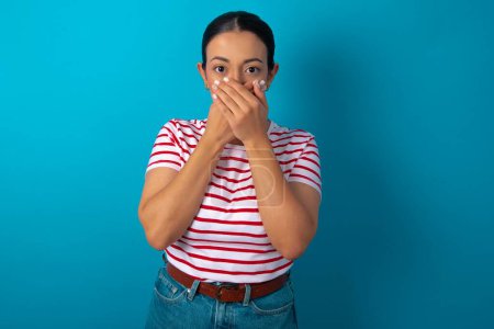 Foto de Mujer molesta que usa una camiseta a rayas, que se cubre la boca con ambas palmas para evitar gritos, después de ver o escuchar algo malo. - Imagen libre de derechos