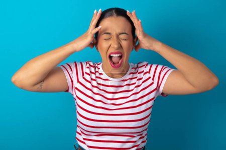 Photo for Shocked panic woman wearing striped T-shirt holding hands on head and screaming in despair and frustration. - Royalty Free Image