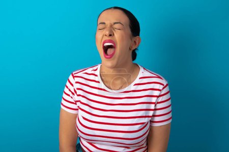 Photo for Stressful woman wearing striped T-shirt screams in panic, closes eyes in terror, keeps hands on head, finds out terrified news, can't believe it. - Royalty Free Image