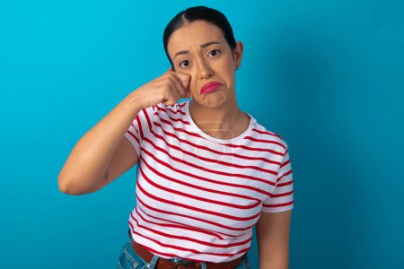 Unhappy woman wearing striped T-shirt crying while posing at camera whipping tears with hand.