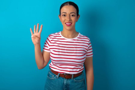 Foto de Mujer vistiendo camiseta a rayas mostrando y señalando hacia arriba con los dedos número cuatro mientras sonríe confiado y feliz. - Imagen libre de derechos
