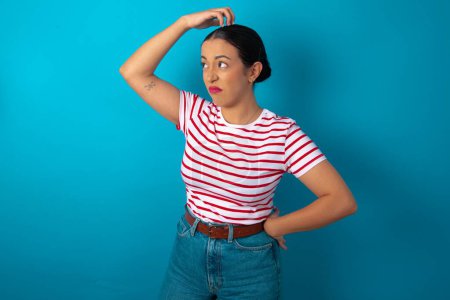 Photo for Woman wearing striped T-shirt saying: Oops, what did I do? Holding hand on head with frightened and regret expression. - Royalty Free Image