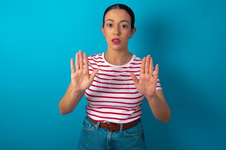 Photo for Woman wearing striped T-shirt doing stop sing with palm of the hand. Warning expression with negative and serious gesture on the face. - Royalty Free Image