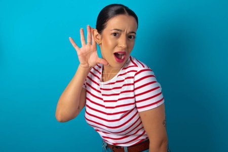 Photo for Oh my God! Funny astonished woman wearing striped T-shirt opening mouth widely looking aside, with hand near ear trying to listen to gossips. - Royalty Free Image
