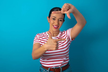 Photo for Positive woman wearing striped T-shirt with cheerful expression, has good mood, gestures finger frame actively at camera. - Royalty Free Image