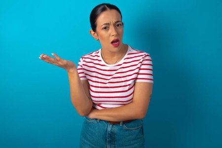 Téléchargez les photos : Studio shot of frustrated woman wearing striped T-shirt gesturing with raised palm, frowning, being displeased and confused with dumb question. - en image libre de droit