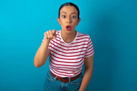 Photo for Shocked woman wearing striped T-shirt points front with index finger at camera and. Surprise and advertisement concept. - Royalty Free Image