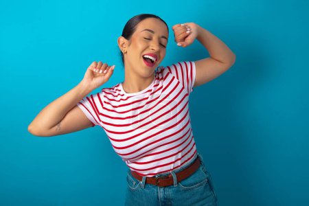 Téléchargez les photos : Femme portant T-shirt rayé relaxant et étirant, bras et mains derrière la tête et le cou souriant heureux - en image libre de droit