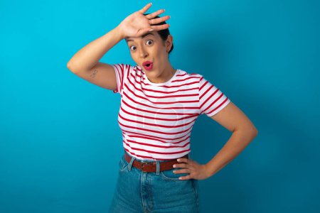 Photo for Woman wearing striped T-shirt wiping forehead with hand making phew gesture, expressing relief feels happy that he prevented huge disaster. It was close enough - Royalty Free Image