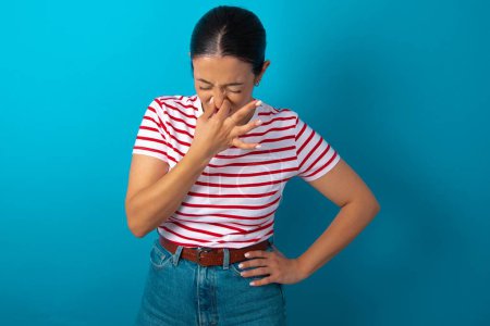 Téléchargez les photos : Femme portant un T-shirt rayé tenant son nez à cause d'une mauvaise odeur. - en image libre de droit