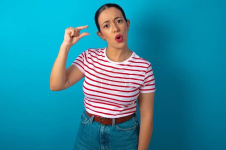 Photo for Shocked woman wearing striped T-shirt shows something little with hands, demonstrates size, opens mouth from surprise. Measurement concept. - Royalty Free Image
