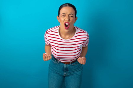 Photo for Joyful excited lucky woman wearing striped T-shirt cheering, celebrating success, screaming yes with clenched fists - Royalty Free Image