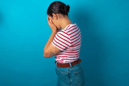 Photo for Sad woman wearing striped T-shirt covering face with hands and crying. - Royalty Free Image