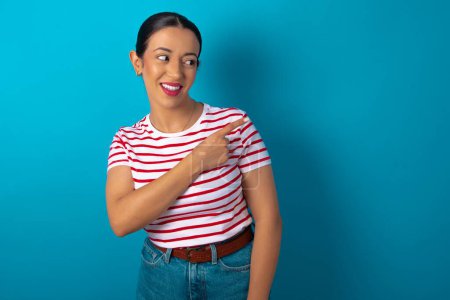Photo for Happy cheerful smiling woman wearing striped T-shirt looking and pointing aside with hand. Copy space and advertisement concept. - Royalty Free Image