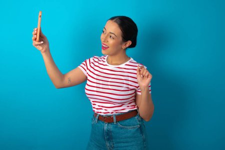 Téléchargez les photos : Portrait d'une femme portant un T-shirt rayé prenant un selfie pour l'envoyer à des amis et disciples ou le poster sur ses médias sociaux. - en image libre de droit