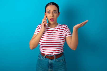 Photo for Woman wearing striped T-shirt talking on the phone stressed with hand on face, shocked with shame and surprise face, angry and frustrated. Fear and upset for mistake. - Royalty Free Image