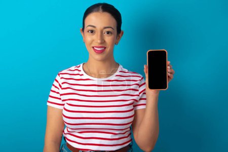 Foto de Mujer sonriente con camiseta a rayas que muestra la pantalla del teléfono vacía. Concepto de publicidad y comunicación. - Imagen libre de derechos
