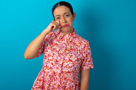 Photo for Disappointed dejected woman wearing floral dress wipes tears stands stressed with gloomy expression. Negative emotion - Royalty Free Image