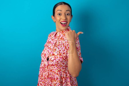 Téléchargez les photos : Femme impressionnée portant une robe florale sur fond bleu studio point de retour espace vide - en image libre de droit
