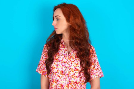 Photo for Side view of young redhead woman wearing floral dress over blue background - Royalty Free Image