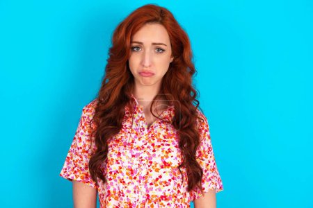 Photo for Redhead woman wearing floral dress over blue background crying desperate and depressed with tears on his eyes suffering pain and depression. Sad facial expression and emotion concept. - Royalty Free Image