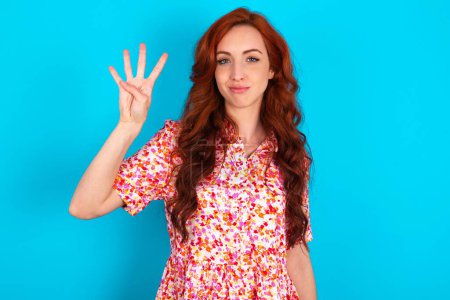 Photo for Redhead woman wearing floral dress over blue background showing and pointing up with fingers number four while smiling confident and happy. - Royalty Free Image