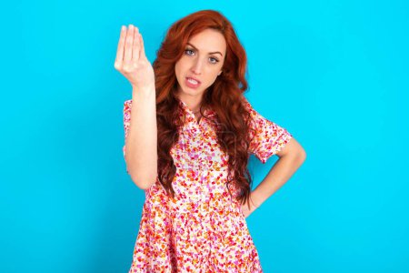 Téléchargez les photos : What the hell are you talking about. Shot of frustrated redhead woman wearing floral dress over blue background gesturing with raised hand doing Italian gesture, frowning, being displeased and confused with dumb question. - en image libre de droit