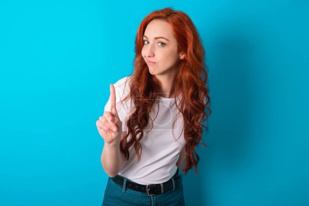Photo for No sign gesture. Closeup portrait unhappy redhead woman wearing white T-shirt over blue background raising fore finger up saying no. Negative emotions facial expressions, feelings. - Royalty Free Image