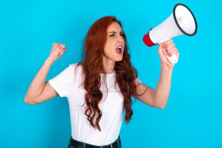 Photo for Redhead woman wearing white T-shirt communicates shouting loud holding a megaphone, expressing success and positive concept, idea for marketing or sales. - Royalty Free Image