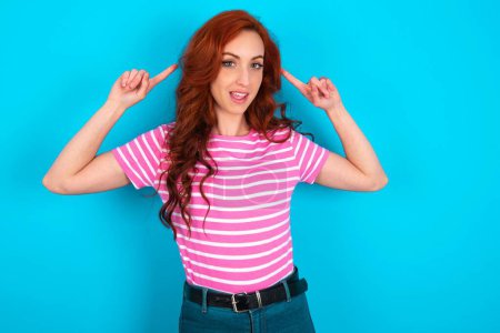 Photo for Cheerful redhead woman wearing pink striped T-shirt over blue background demonstrating hairdo - Royalty Free Image