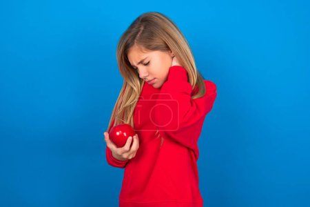Photo for Beautiful caucasian teen girl wearing red sweatshirt over blue background suffering from neck ache injury, touching neck with hand, muscular pain. - Royalty Free Image