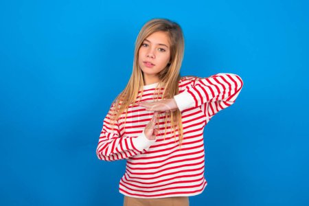 Photo for Teen girl wearing striped shirt over blue background feels tired and bored, making a timeout gesture, needs to stop because of work stress, time concept. - Royalty Free Image