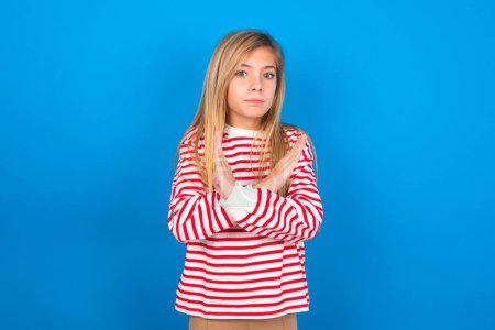 Photo for Teen girl wearing striped shirt over blue background has rejection angry expression on face and crossing hands doing refusal negative sign. - Royalty Free Image