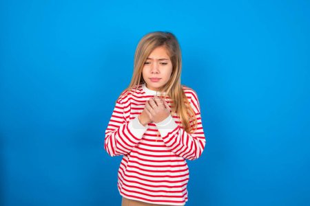 Téléchargez les photos : Triste adolescente portant une chemise rayée sur fond bleu se sentant bouleversée tout en passant du temps seul à la maison à regarder la caméra avec un regard malheureux ou regrettable. - en image libre de droit