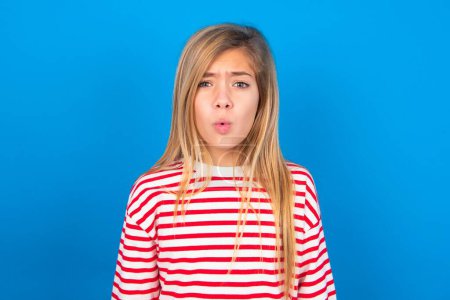 Photo for Teen girl wearing striped shirt over blue background expressing disgust, unwillingness, disregard having tensive look frowning face, looking indignant with something. - Royalty Free Image