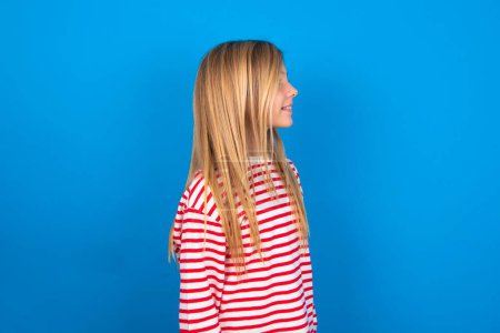 Photo for Profile of smiling teen girl wearing striped shirt over blue background with healthy skin, has contemplative expression, ready to have outdoor walk. - Royalty Free Image
