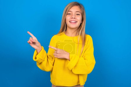 Téléchargez les photos : Caucasien adolescent fille portant pull jaune sur les points muraux bleus à l'espace de copie indique pour la publicité donne la bonne direction - en image libre de droit