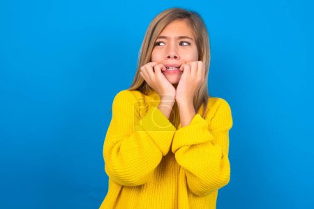 Photo for Terrified caucasian teen girl wearing yellow sweater on blue background - Royalty Free Image