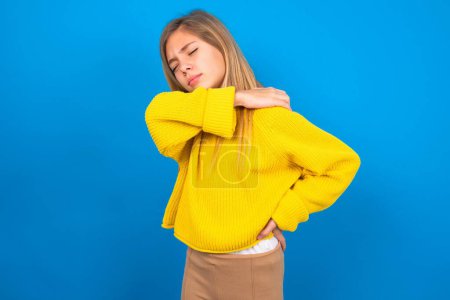 Photo for Beautiful caucasian teen girl wearing yellow sweater over blue wall got back pain - Royalty Free Image