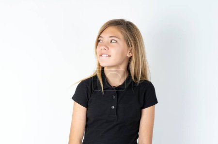 Foto de Amazed caucásico adolescente chica usando negro camiseta sobre blanco pared mordiendo labio y buscando difícil de espacio vacío - Imagen libre de derechos